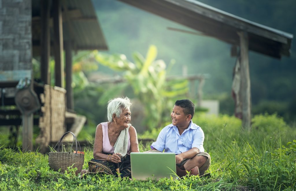 Alte asiatische Frau sitzt mit jungem asiatischen Bub in der Wiese vor einem Laptop