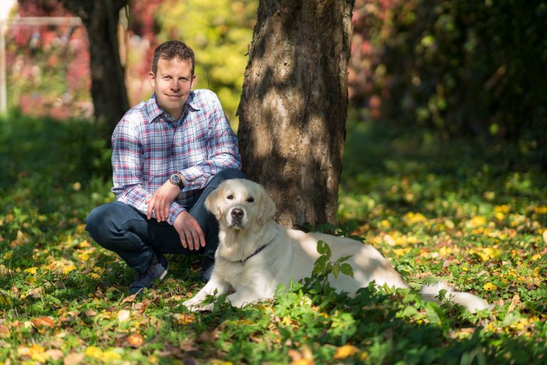 Kris Lenart hockt mit Hund im Schatten eines Baumes