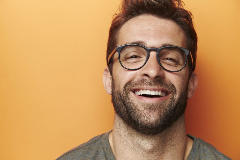 Mann mit schönen Zähnen und Brille lacht vor orangem Hintergrund
